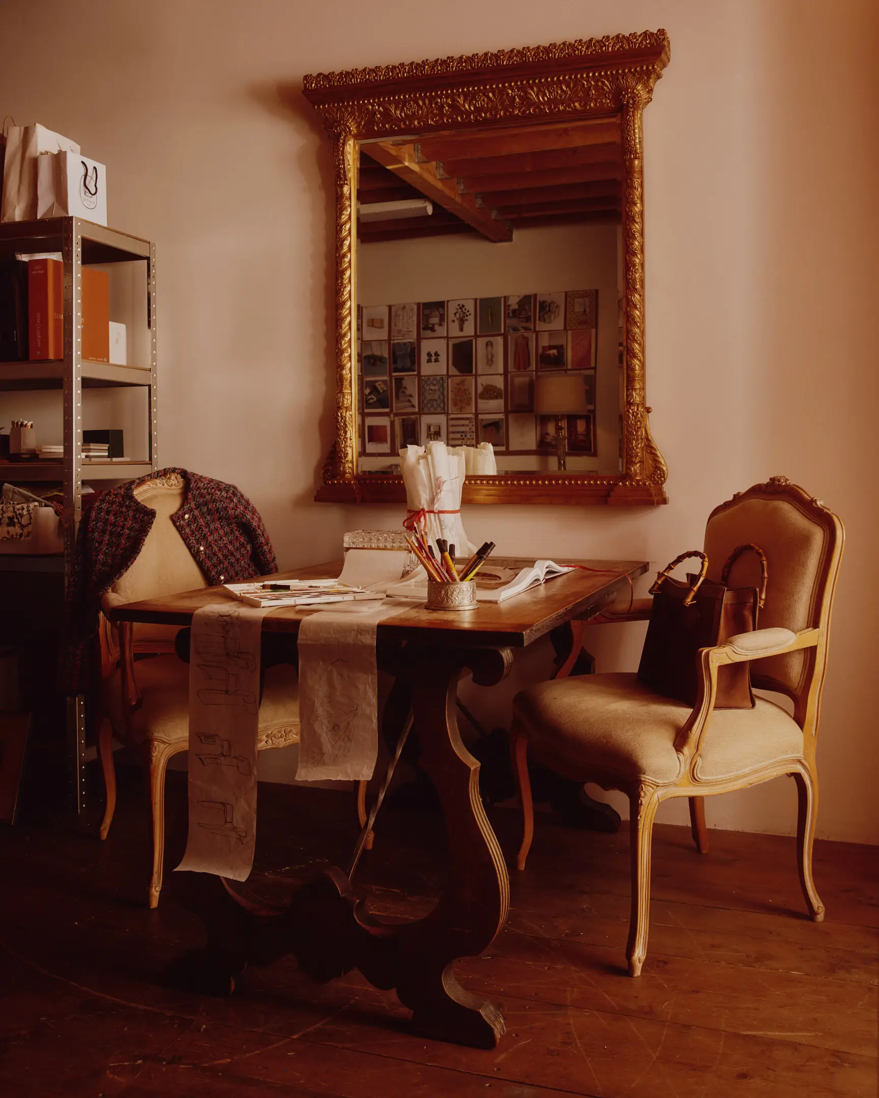 A table with drawing materials, Hermes purse, and jacket with an ornate mirror, and studio shelving in the background. The studio of Lulu LaFortune, a designer based in Los Angeles, Ca. Shot originally for House Beautiful publication. 