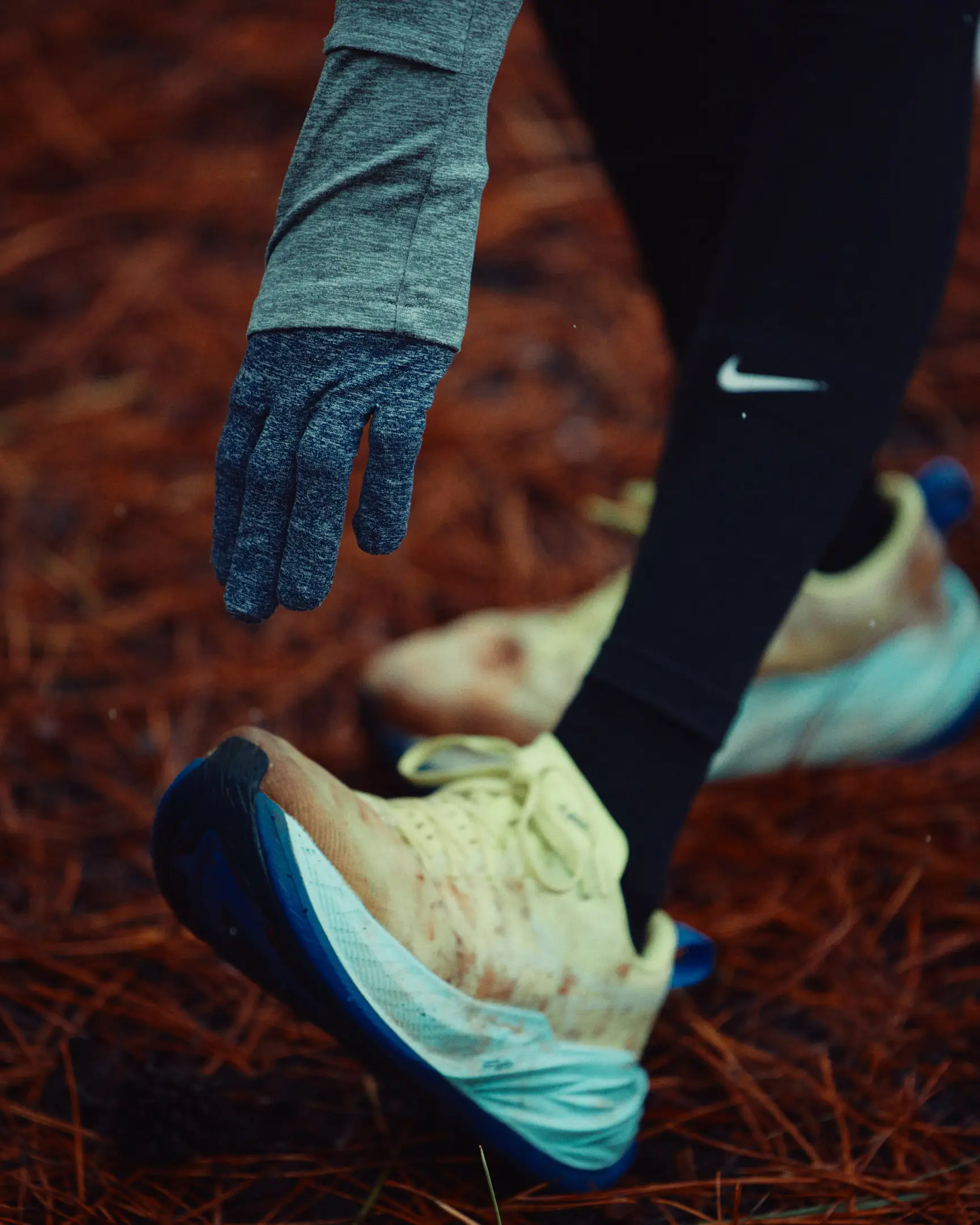 Athlete stretching in a snowy forrest, wearing blue gloves, black Nike leggings, and neon colored Asics running shoes. Dream Run Camp features the running camp hosted by Michael Fitzgerald, a runner living with long covid, that's hosted in Flagstaff, AZ. This commission was originally commissioned by The New York Times.