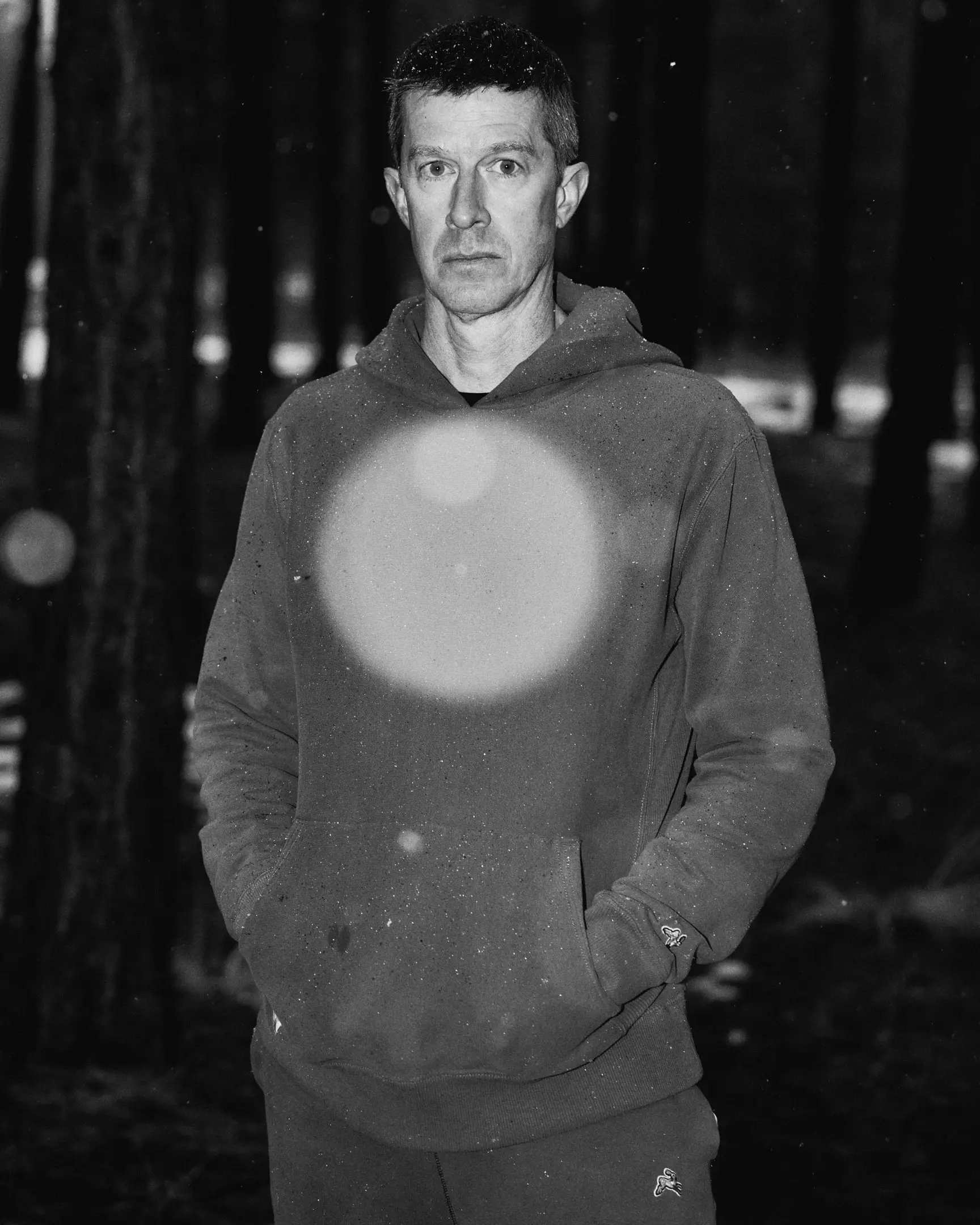 A posed portrait of Michael Fitzgerald within a snowy forest. The black and white photograph capturesFitzgerald in black and white set against falling snow. The flash captures a snow flake falling directly in the center of the image. Dream Run Camp features the running camp hosted by Michael Fitzgerald, a runner living with long covid, that's hosted in Flagstaff, AZ. This commission was originally commissioned by The New York Times.